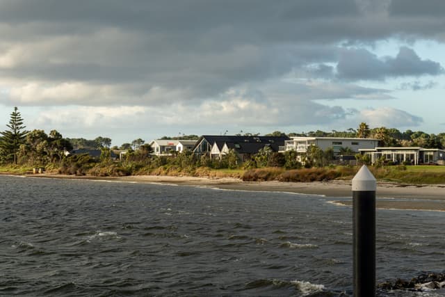 water ocean sea shore beach coast clouds sky buildings houses trees greenery landscape pier pole overcast gray blue