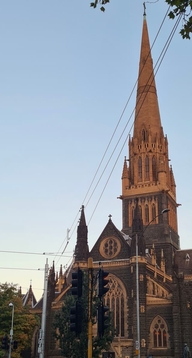 Church Spire Architecture Gothic Building Tower Sky Blue Stone Windows Trees Cross Steeple Historic Landmark Religion Structure Exterior Facade Design Urban Cityscape Sunset Shadows Roof Details Arches Columns Wires