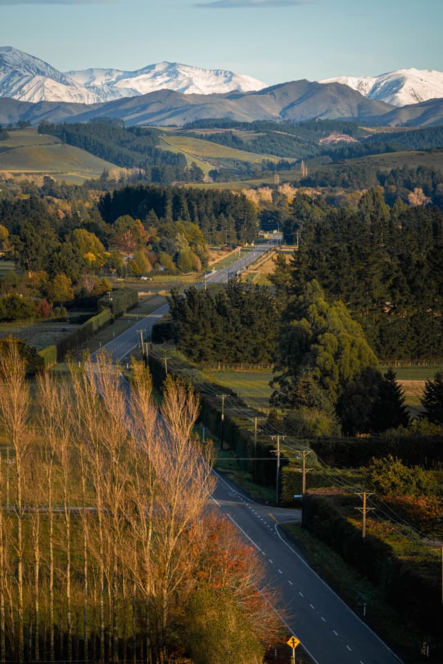 landscape mountains snow trees road forest hills sky nature scenery outdoors rural countryside horizon green blue brown white fields vegetation pathway travel serene peaceful panoramic scenic vista