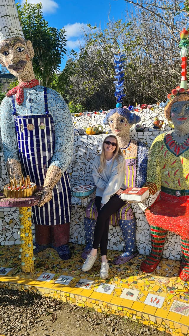 sculpture mosaic art people figures colorful blue sky trees outdoor bench sitting sunglasses hat apron red yellow green tiles stone