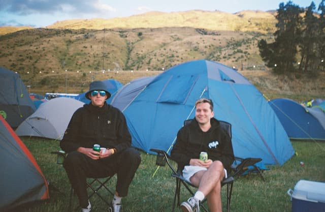 tents camping chairs people grass mountains trees sky blue outdoor nature landscape relaxation leisure festival