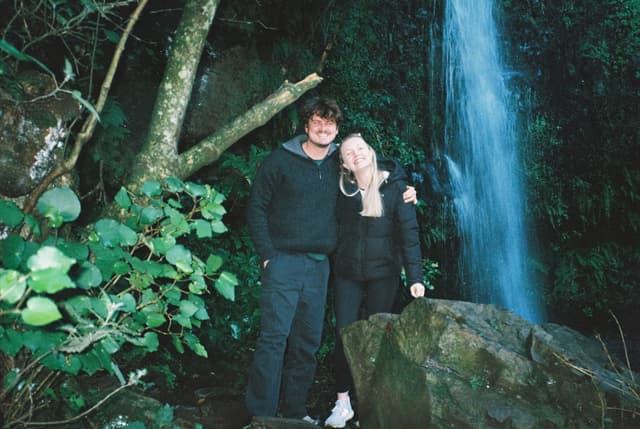 waterfall nature forest greenery rocks trees couple smiling black clothing blue water stone leaves outdoors primary green