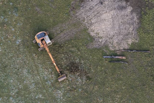 excavator construction machinery digger earth dirt grass field aerial view equipment vehicle yellow green brown landscape site work industrial outdoor digging machine