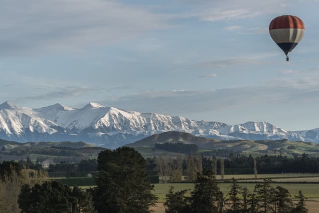 hot air balloon mountains snow trees landscape sky clouds green blue white forest field horizon travel adventure nature outdoor scenic serene peaceful exploration altitude flight aerial view panorama tranquility beauty majestic wilderness rural countryside