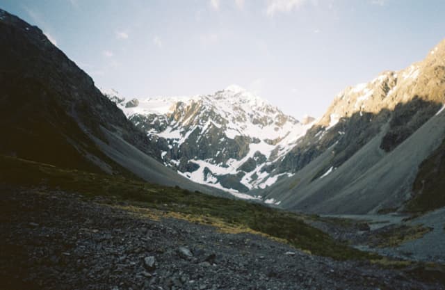 mountains snow peaks valley rocks sky clouds landscape nature outdoor scenery sunlight shadow green grass blue