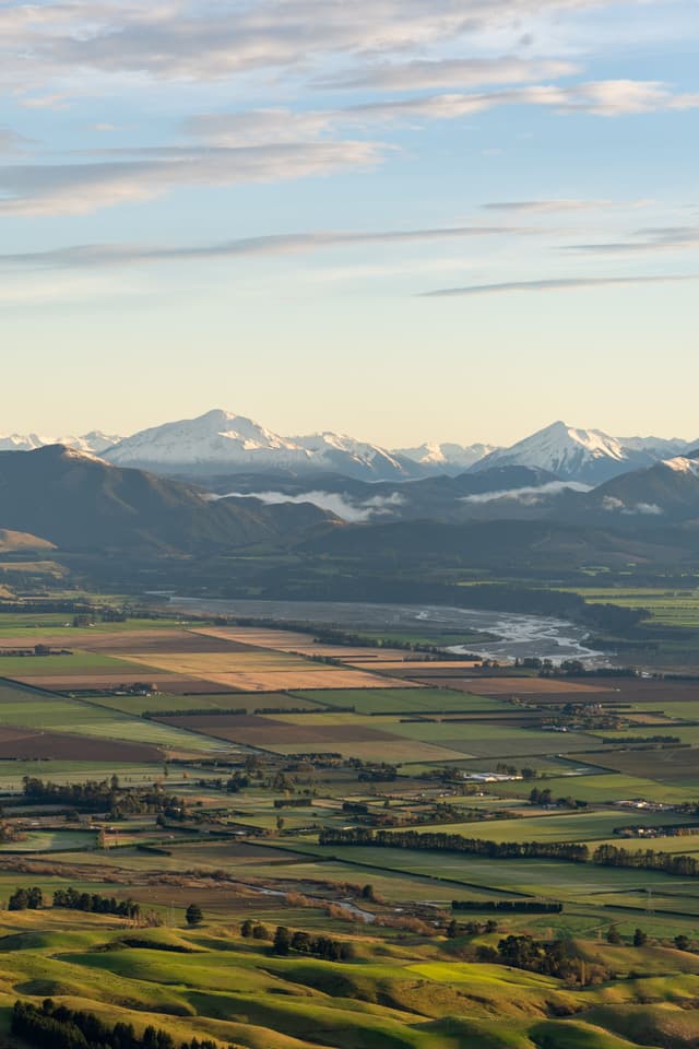 landscape mountains fields sky clouds snow valley hills greenery horizon nature scenic panorama rural agriculture blue green white sunlight peaceful serene vast open space distant peaks plains farmland countryside tranquility