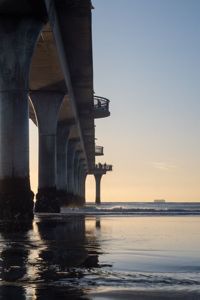 pier ocean water reflection sunset sky horizon structure columns waves beach silhouette ship blue