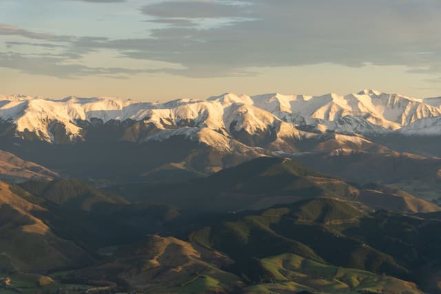 mountains snow peaks landscape sky clouds horizon sunlight shadows green white blue nature scenery panoramic outdoor majestic serene tranquil rugged natural beauty elevation terrain wilderness alpine vista breathtaking picturesque remote peaceful vast expansive dramatic impressive stunning awe-inspiring primary-color-white