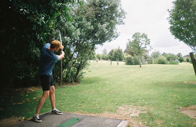 golf golfer swing club course grass trees sky outdoors green blue shorts shoes tee sports action summer nature landscape game recreation leisure activity