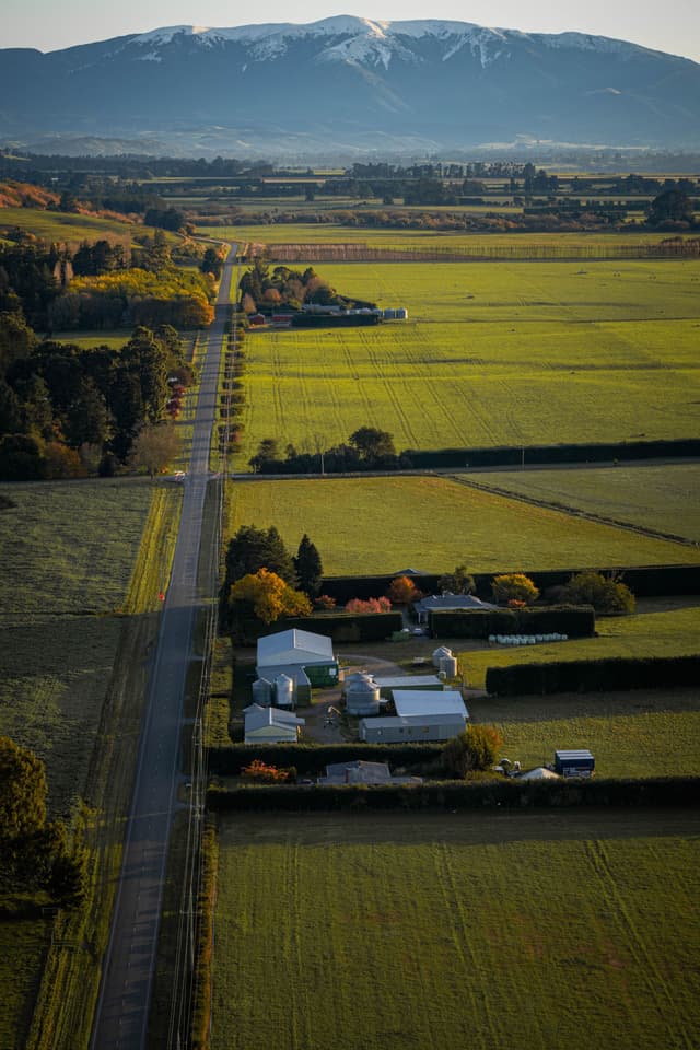 landscape road fields farm buildings trees mountains sky green yellow blue snow horizon rural nature agriculture scenery countryside aerial view