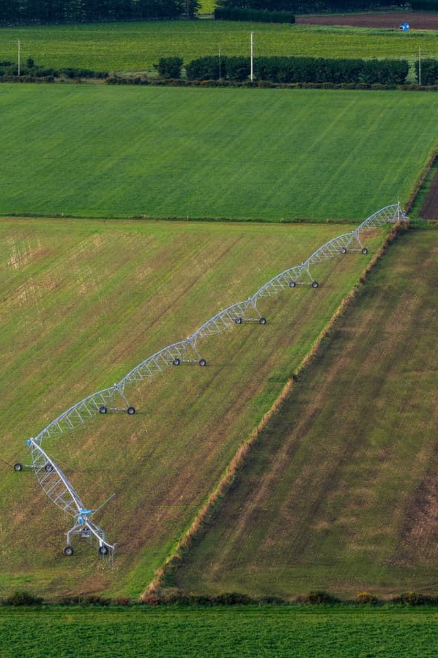 Field Farmland Irrigation System Pivot Green Grass Crops Agriculture Farming Machinery Equipment Wheels Structure Aerial View Landscape Rural Countryside Vegetation Lines Patterns Rows Watering System Technology Outdoors Environment Growth Cultivation Harvesting Blue Sky