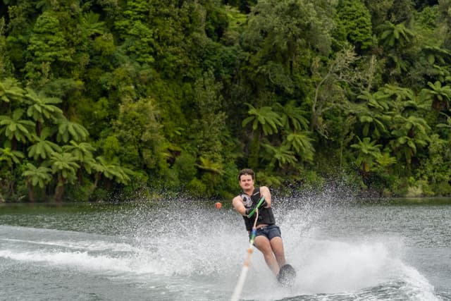 waterskiing water skier splash lake forest trees greenery motion action outdoor sport lifejacket rope speed wave nature adventure summer activity fun excitement balance skill aquatic recreation landscape environment green white blue thrill adrenaline movement skillful athletic challenge coordination concentration focus determination energy dynamic vibrant scenery background natural setting leisure hobby pursuit enjoyment pastime physical fitness challenge excitement primary color green