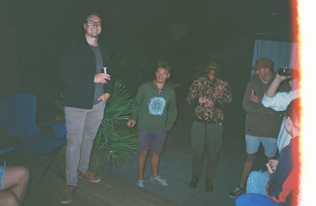 People Standing Group Night Dark Clothing Plants Chairs Blue Red Light Casual Outdoor Social Gathering