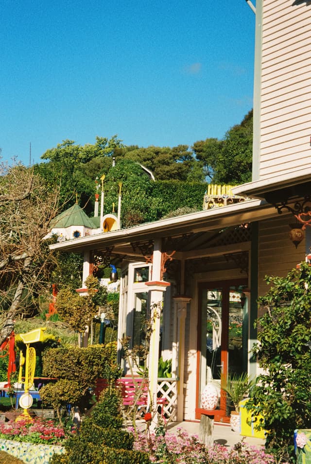 house garden porch plants trees sky blue roof windows door columns bushes flowers sunlight architecture outdoor greenery fence path shrubs colorful vibrant exterior building landscape yard