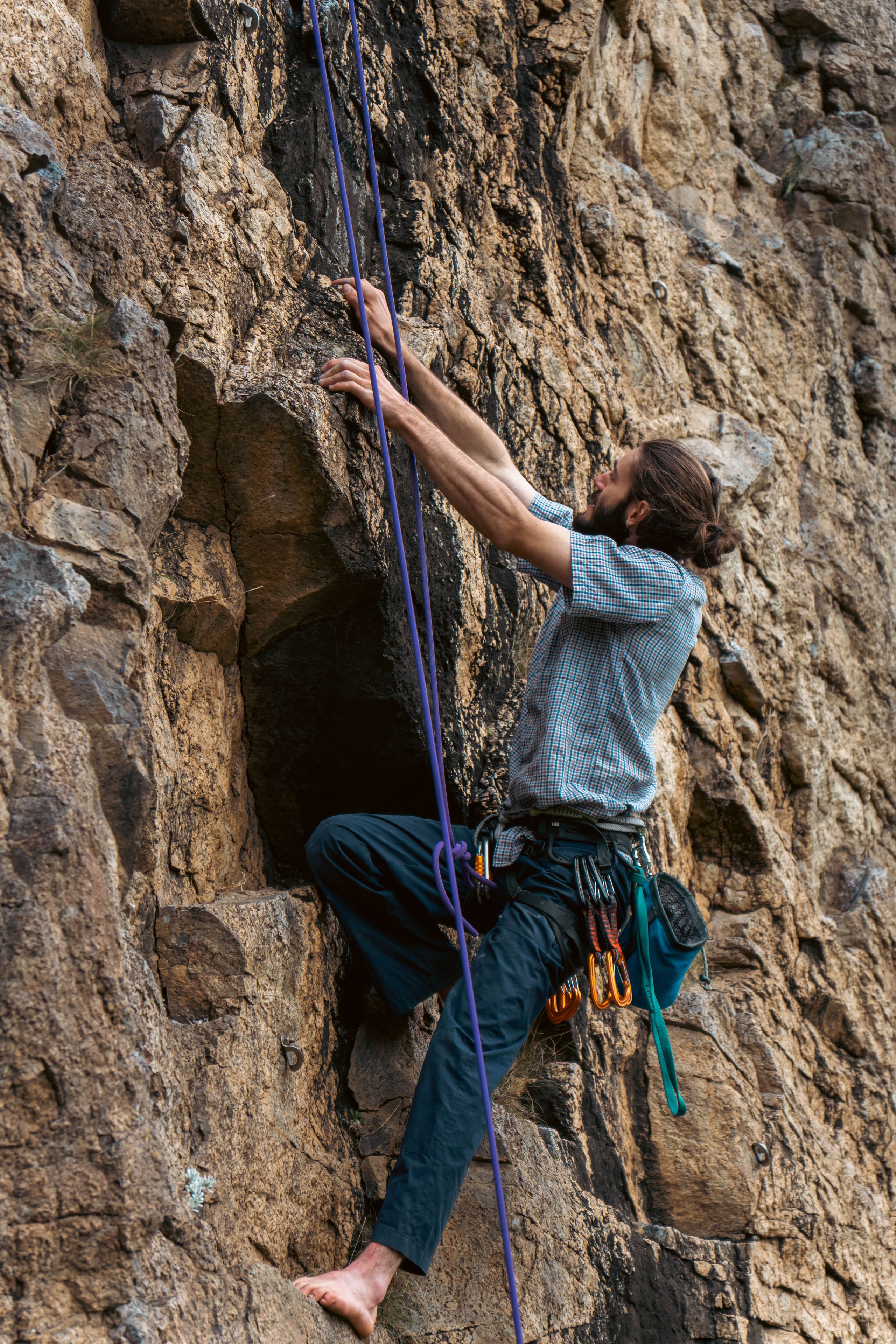Climbing Rock Climber Rope Wall Gear Harness Shoes Outdoors Adventure Sport Nature Brown Blue Gray Rugged Cliff Vertical Ascent Challenge Strength Focus Determination Safety Equipment Physical Activity Effort Concentration Movement Skill