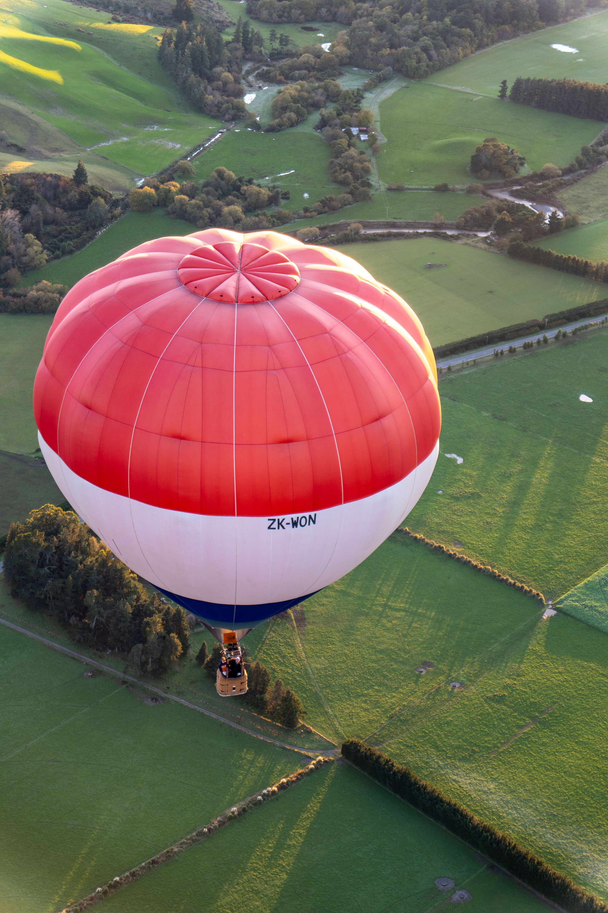Hot air balloon Balloon Red White Blue Sky Basket Fields Trees Landscape Aerial view Grassland Countryside Flight Adventure Travel Scenic Horizon Shadows Sunrise Morning Nature Outdoors Airborne Altitude Perspective Patchwork Green