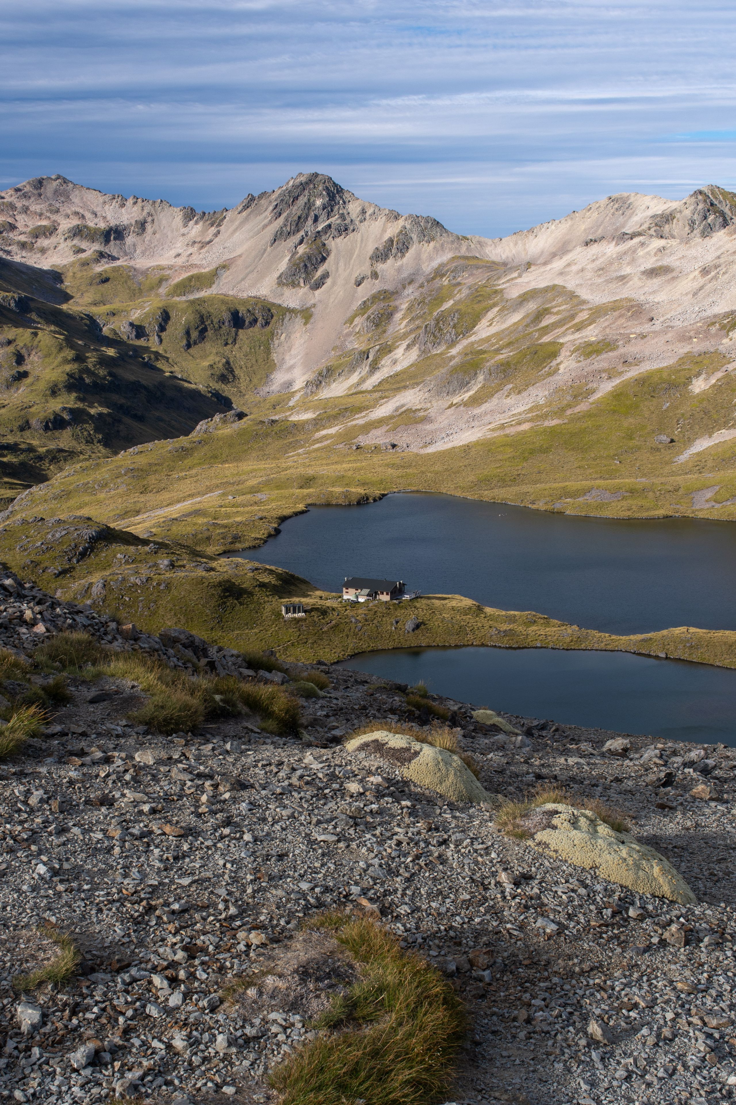 mountains lake rocks grass sky clouds landscape nature outdoor scenery blue green brown rugged terrain peaks hills water reflection remote serene peaceful wilderness alpine