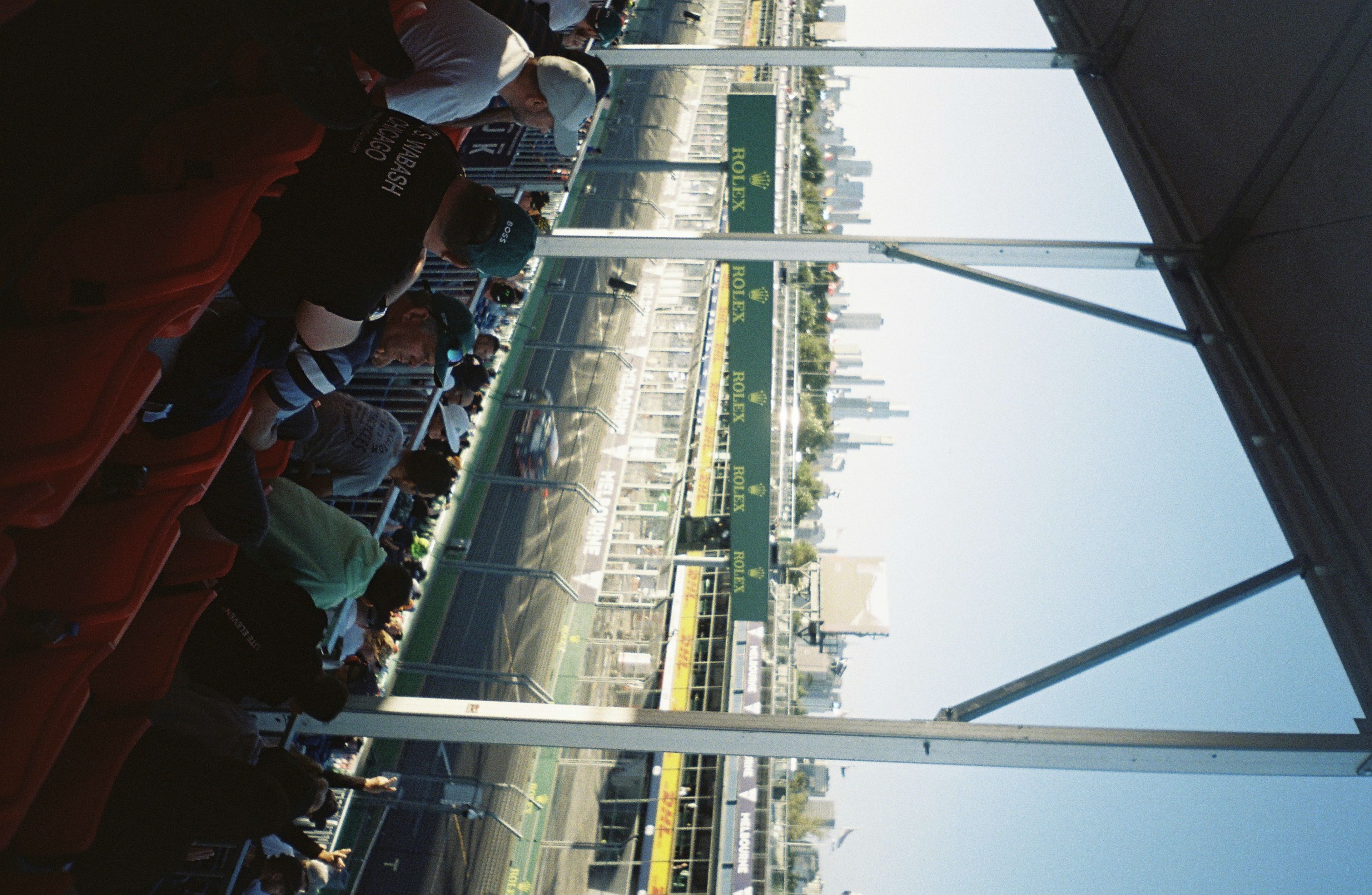 stadium race track spectators grandstand city skyline buildings sky blue seats people event outdoor architecture railing urban sports daytime