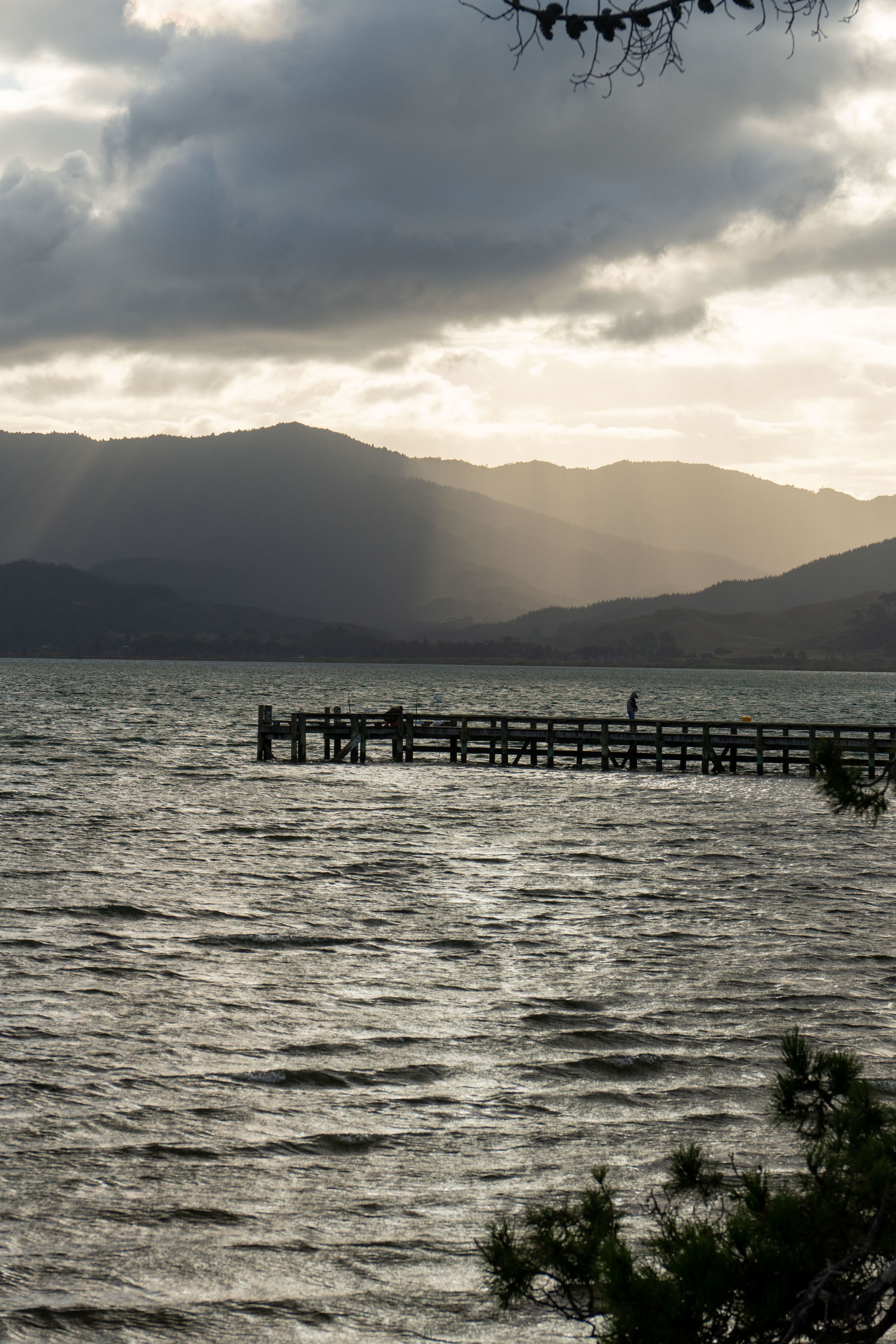 lake water pier dock mountains hills clouds sky sunset silhouette landscape nature outdoor scenery reflection horizon tree branches gray