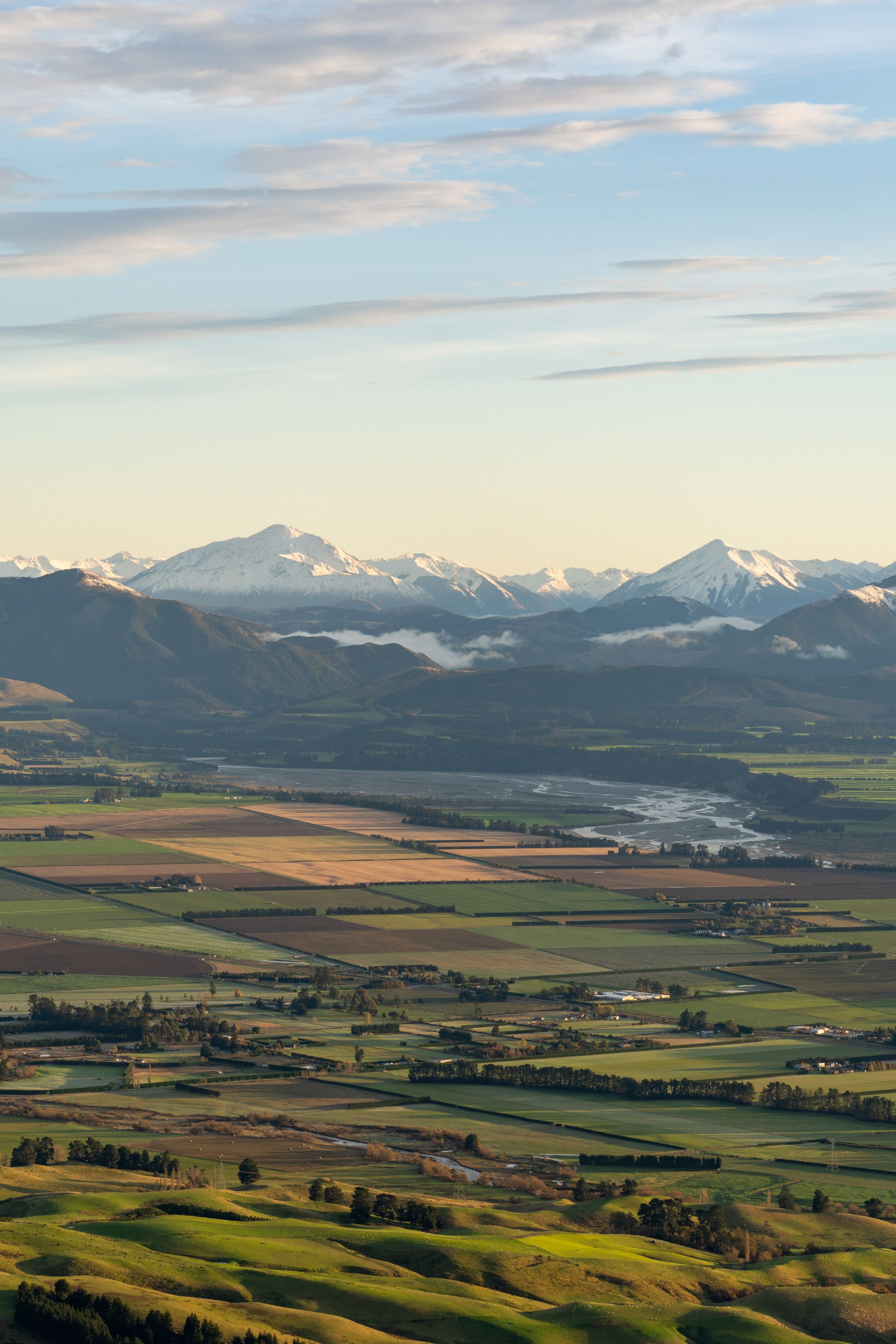 landscape mountains fields sky clouds snow valley hills greenery horizon nature scenic panorama rural agriculture blue green white sunlight peaceful serene vast open space distant peaks plains farmland countryside tranquility