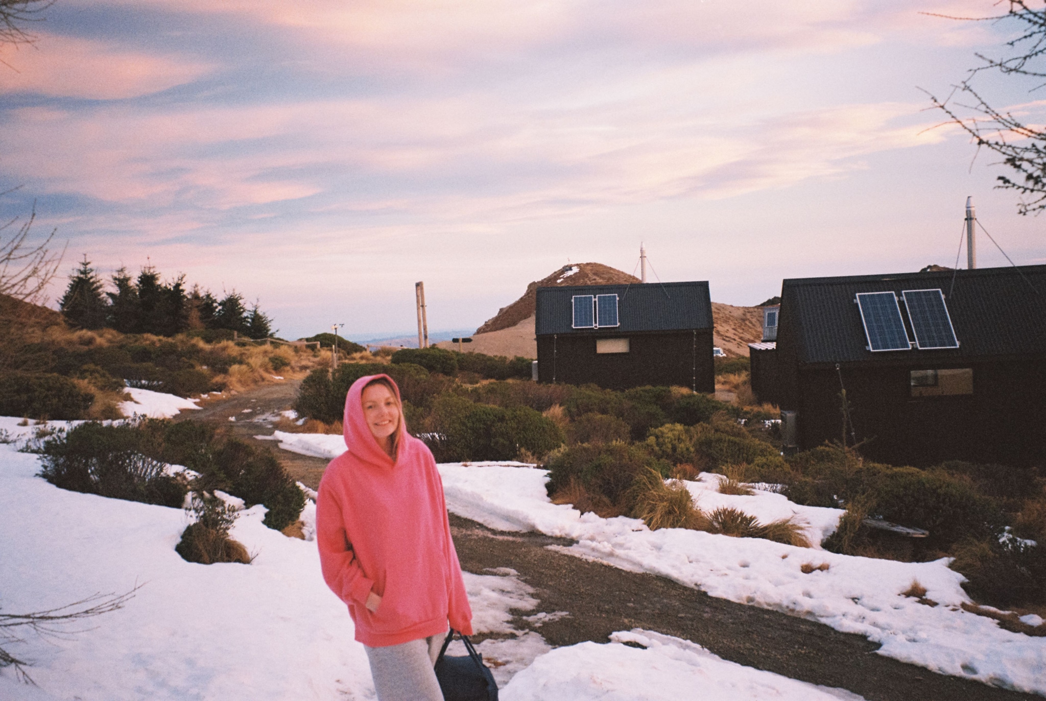 snow person pink hoodie path cabin solar panels sky clouds sunset landscape winter outdoor nature primary color pink
