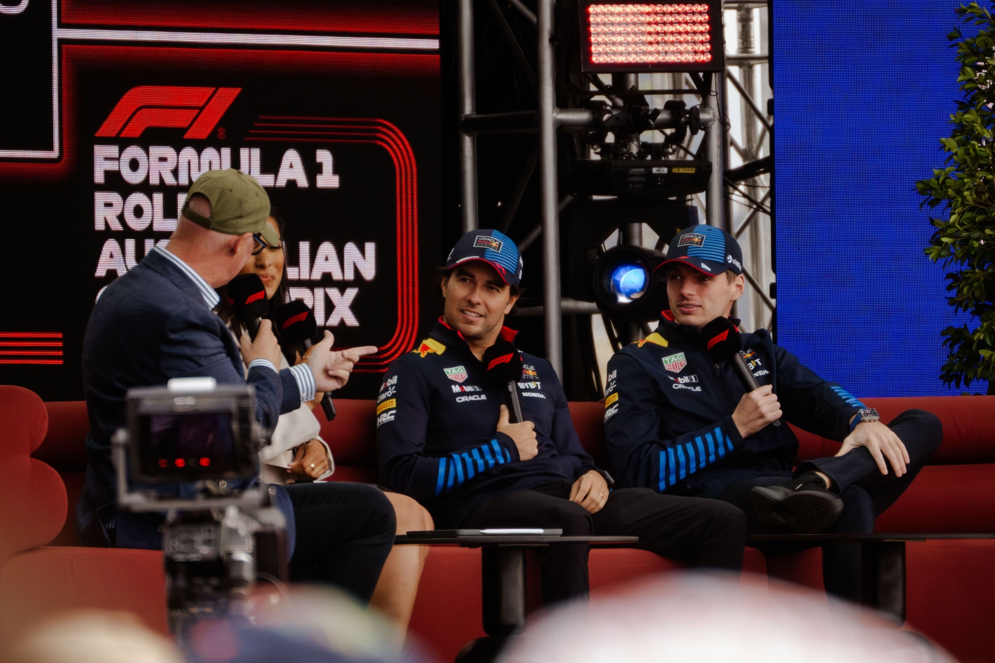 F1 Formula 1 Australian Grand Prix interview stage microphones caps jackets logos red blue black chairs people audience screens plants lights conversation event sports racing discussion panel