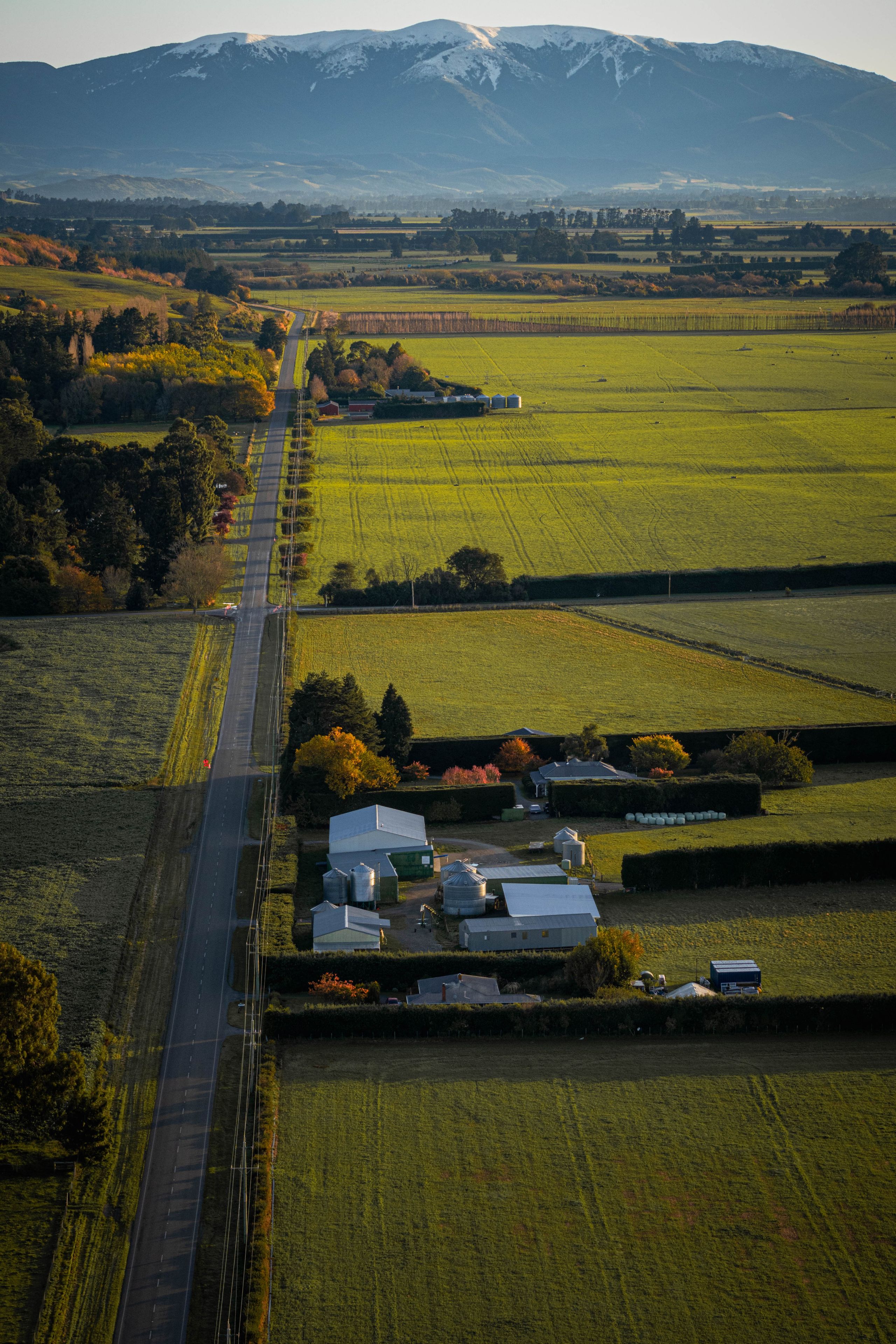 landscape road fields farm buildings trees mountains sky green yellow blue snow horizon rural nature agriculture scenery countryside aerial view