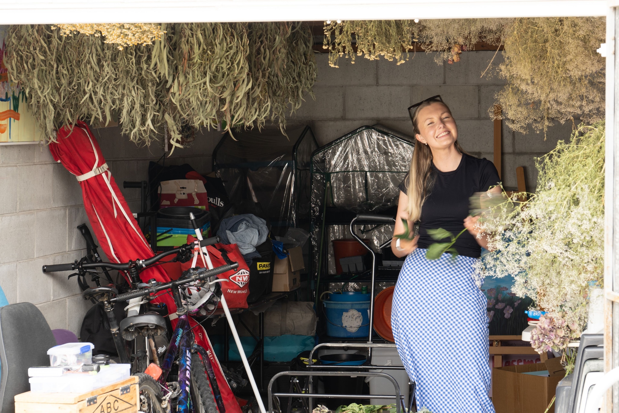 garage bicycle plants woman drying flowers storage boxes red blue green black gray white shelves tools equipment ceiling wall floor