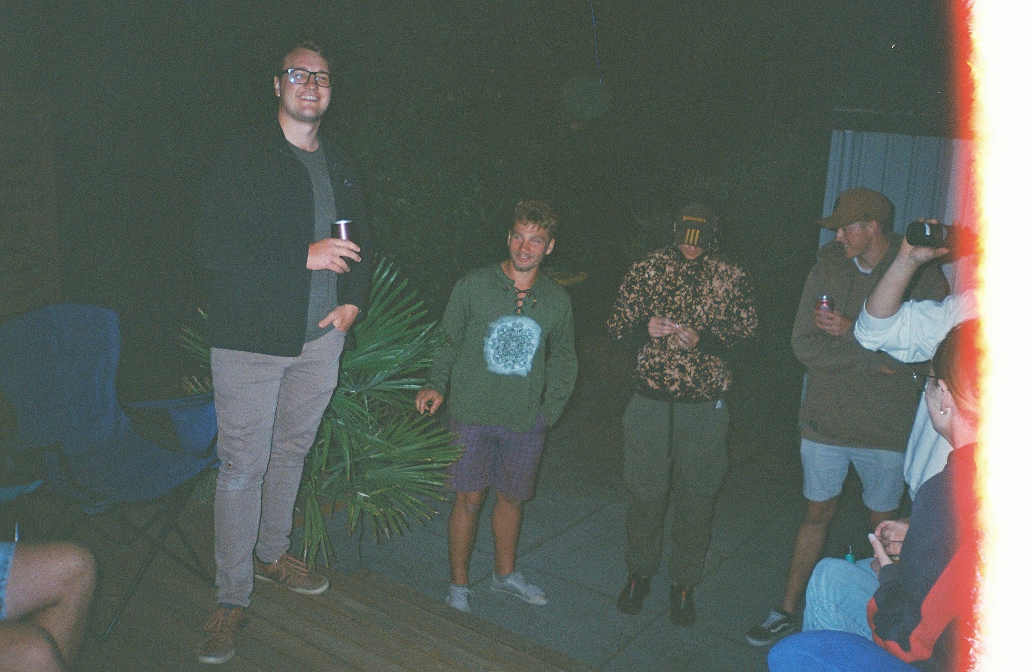 People Standing Group Night Dark Clothing Plants Chairs Blue Red Light Casual Outdoor Social Gathering